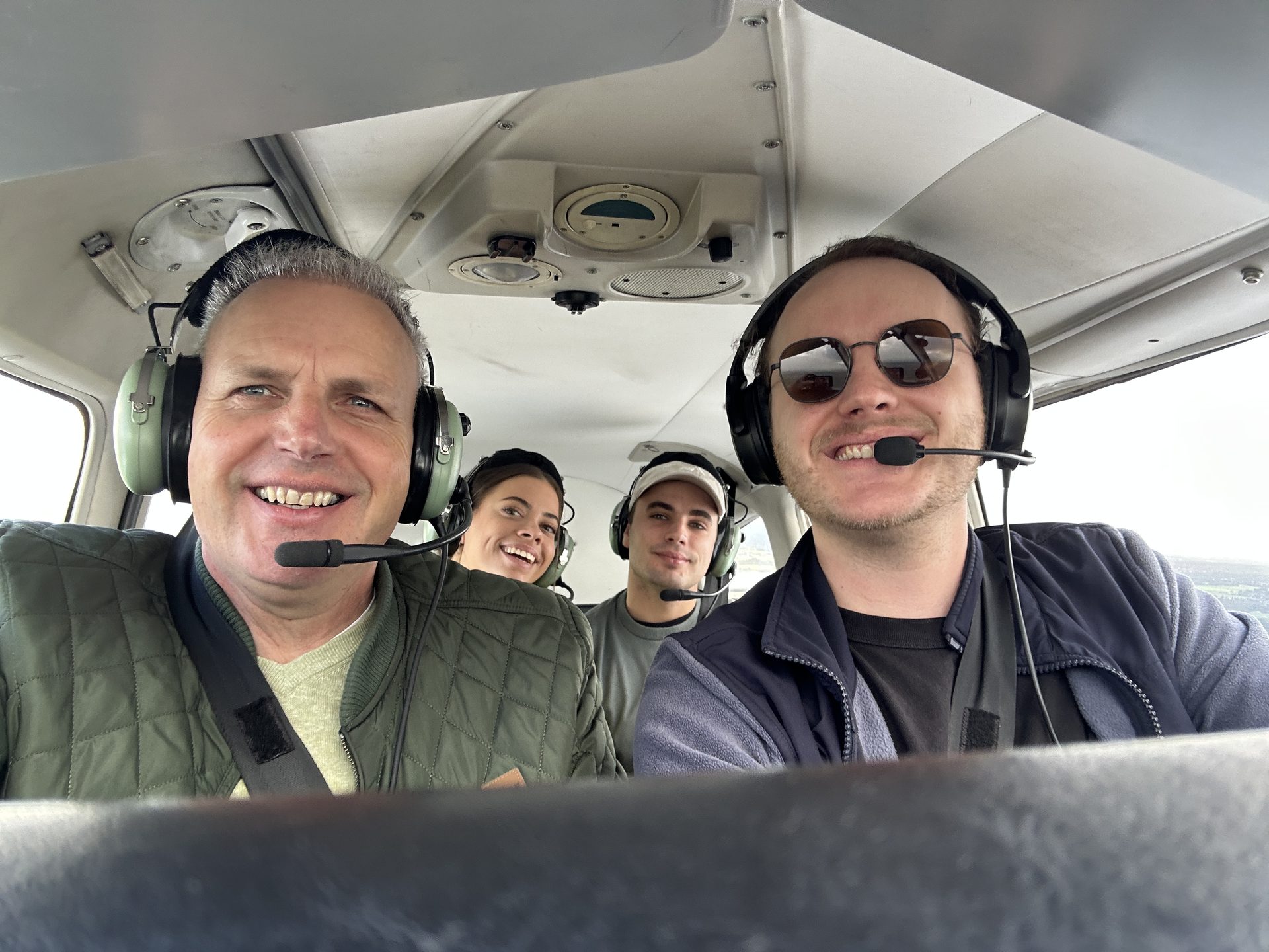 Vier meevliegers met headsets en glimlach in de cabine van de Piper tijdens een rondvlucht boven Nederland