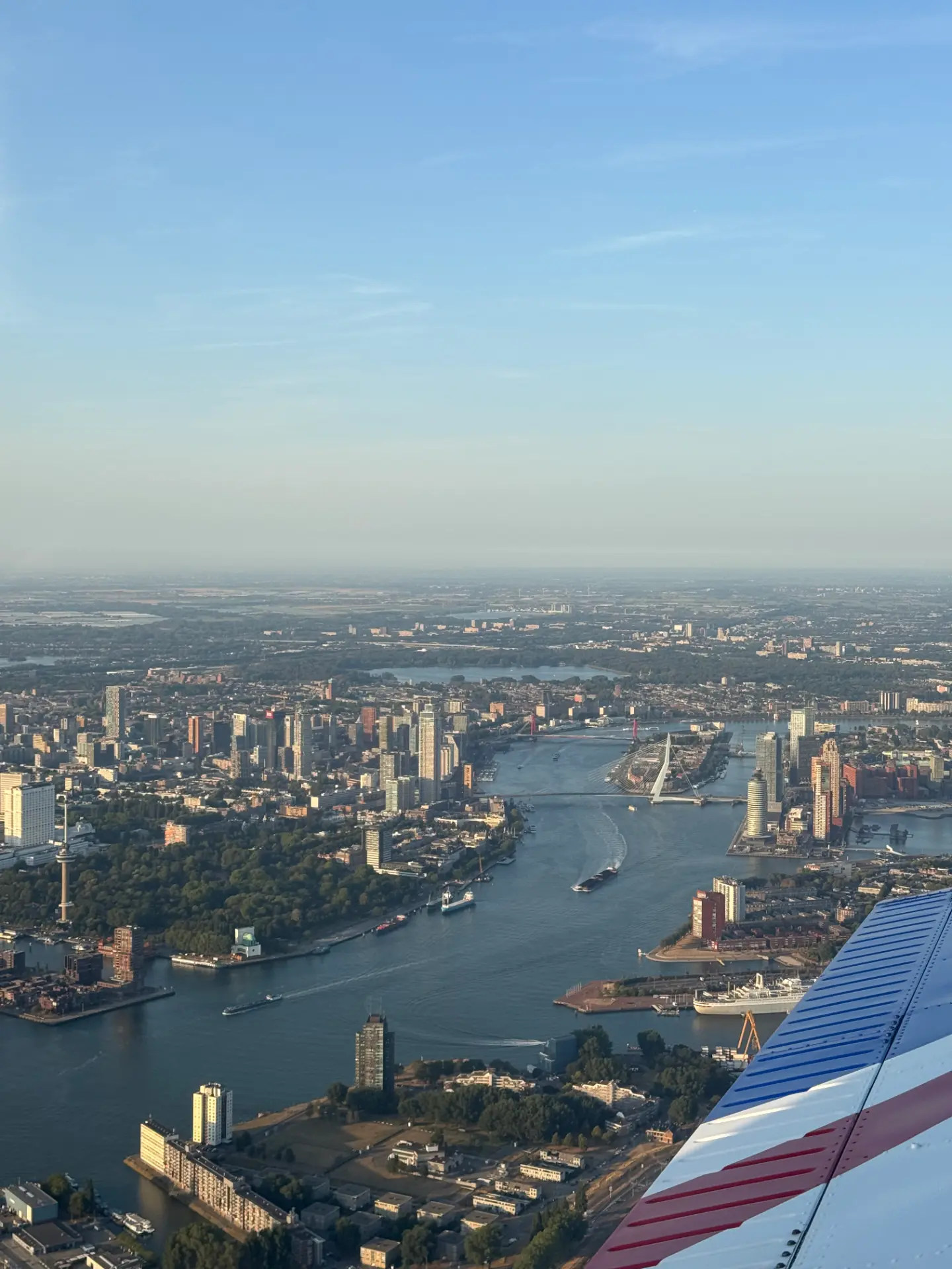 Luchtfoto van de Rotterdamse skyline met de Erasmusbrug en de Maas, gezien over de vleugel van de Piper tijdens een sightseeing vlucht