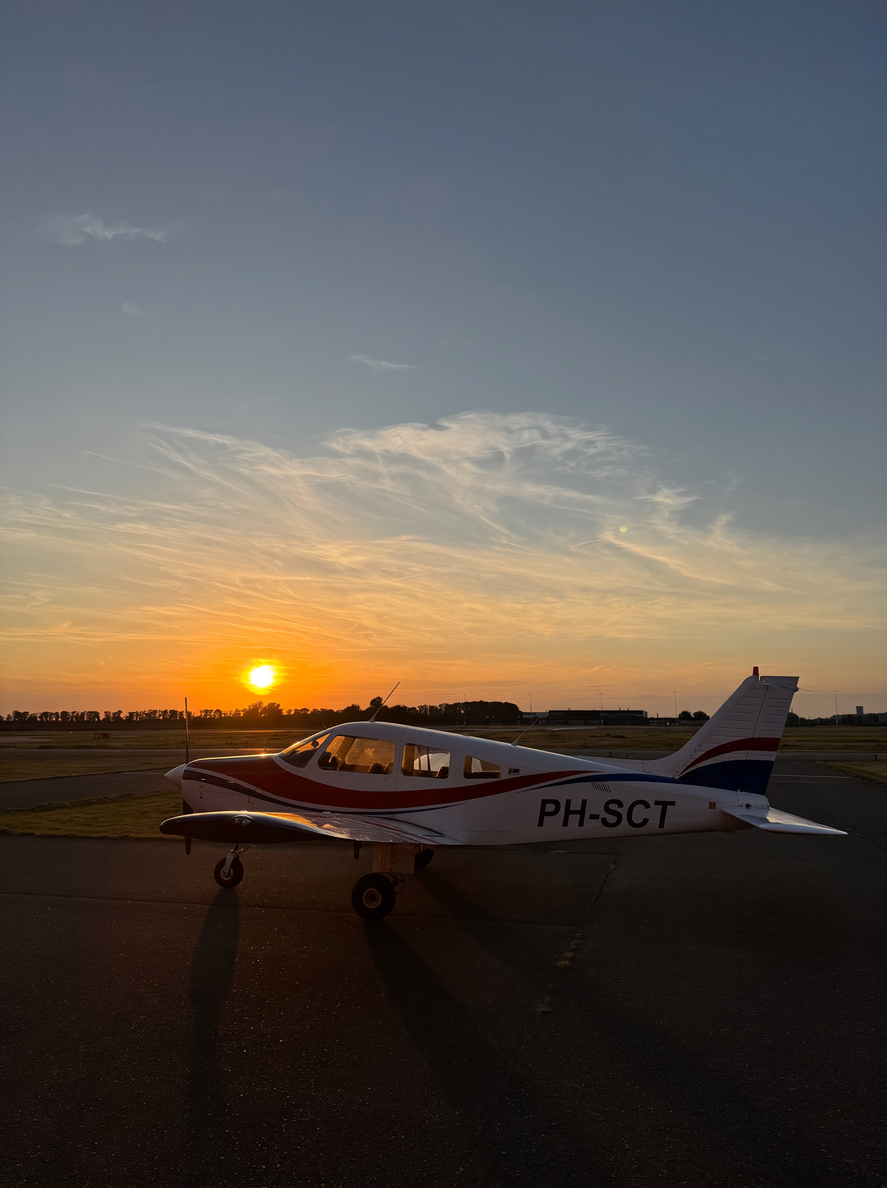 Zijaanzicht van de Piper PA-28 Warrior II tegen een oranje avondlucht op Lelystad Airport